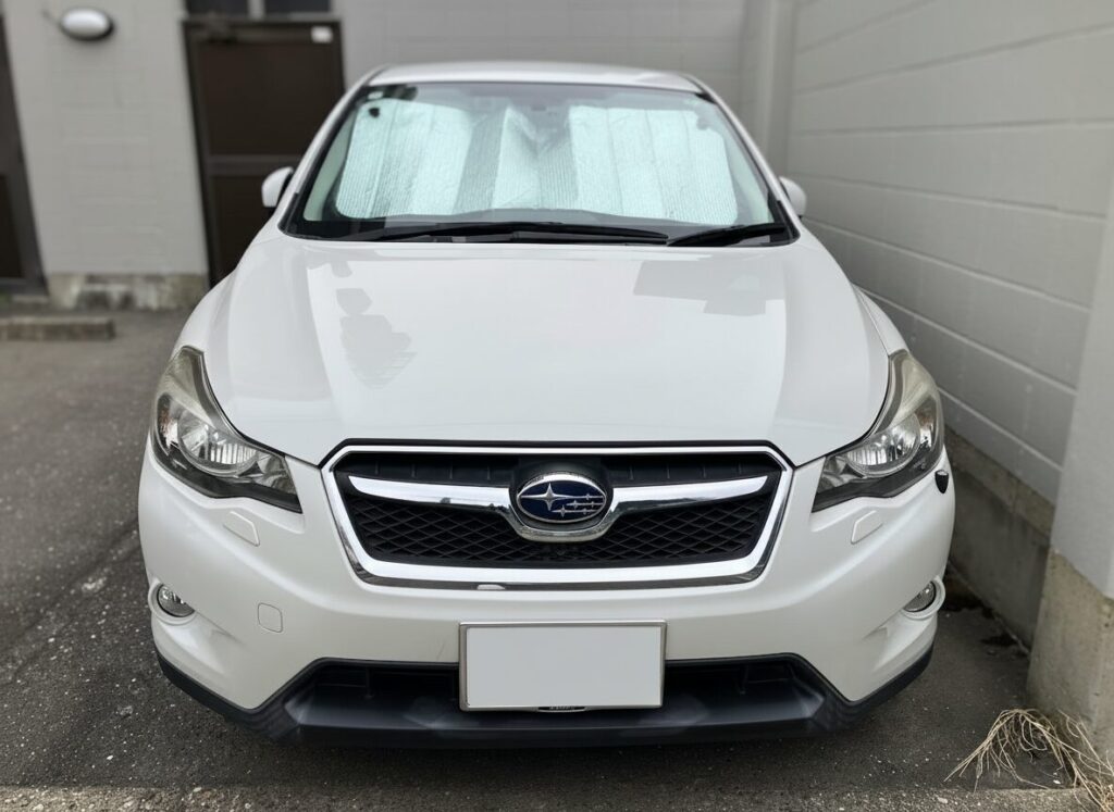 White Subaru SUV seen from the front with a sunshade visible through the windshield and a chrome grille center badge.