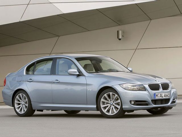 Silver BMW 3 Series sedan parked on a paved surface beside a modern, angular building exterior.