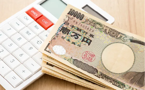 お金 | 車買取のソコカラ Stack of Japanese yen banknotes fanned on a white calculator, suggesting money calculation.
