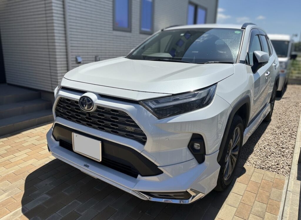Front-left angle of a white SUV parked on a brick driveway beside a modern gray building, showing the grille and headlights accurately.