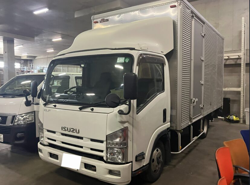 White Isuzu box truck with a refrigerated cargo area parked in an indoor warehouse garage.