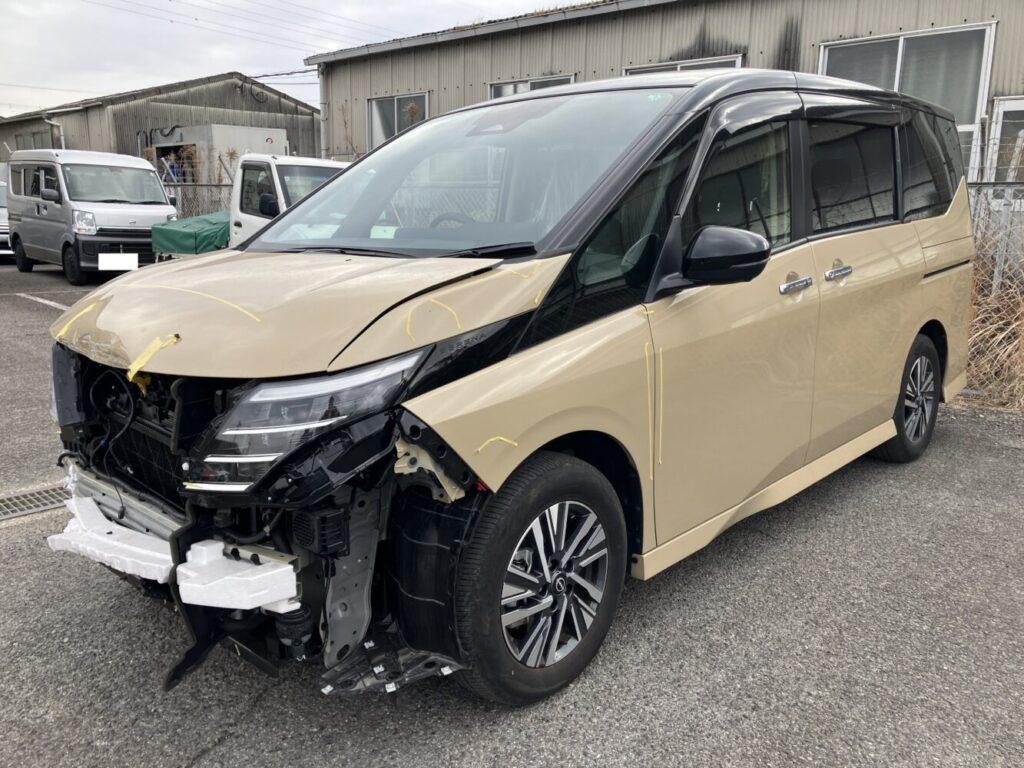 IMG_7527 | 車買取のソコカラ Beige minivan with severe front-end damage exposing the engine; bumper and grille are missing.