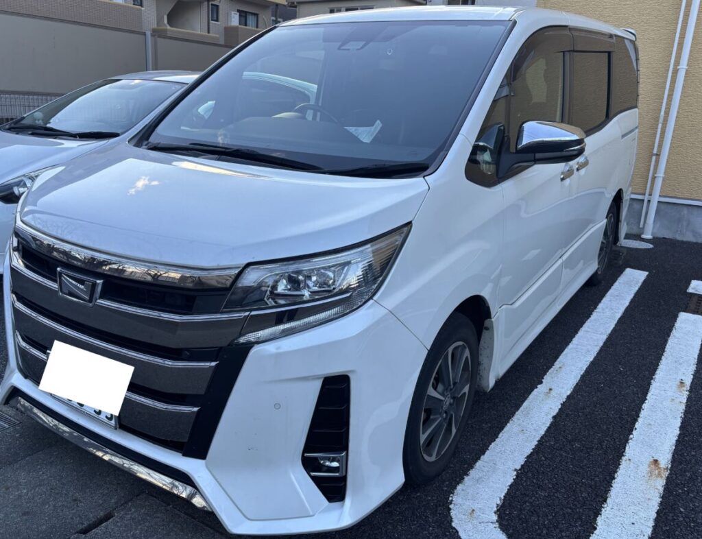 White minivan parked in a marked space, viewed from the front-left with a chrome grille and prominent headlights.