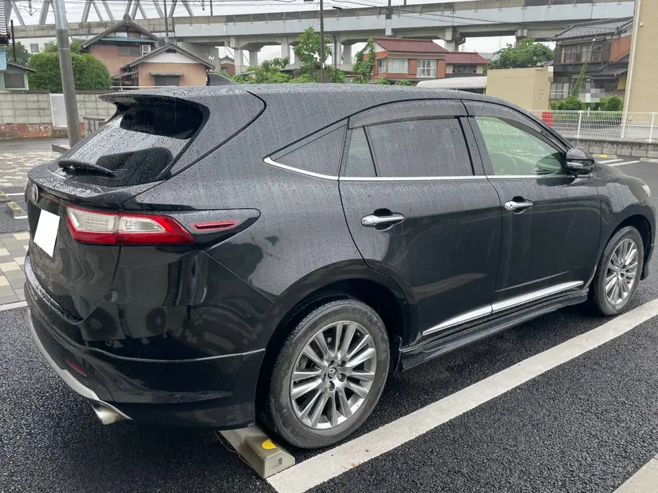 ハリアー買取事例_2017年式 | 車買取のソコカラ Black SUV parked in a rain-soaked parking lot, rear three-quarter view with chrome window trim, alloy wheels, roof spoiler, and a white license plate.