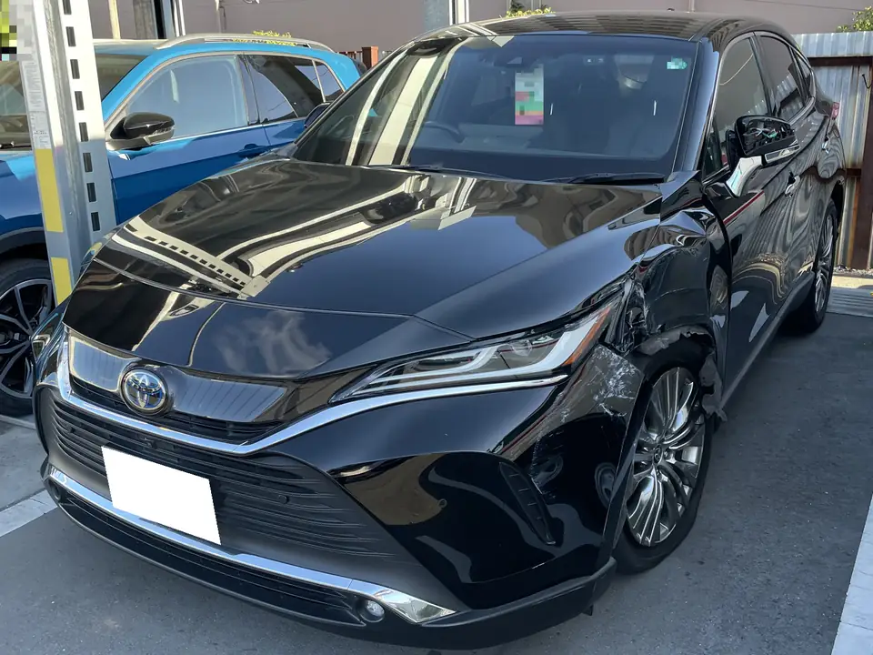ハリアー買取事例_2021年式_事故車 | 車買取のソコカラ Black Toyota sedan with front-right damage, parked in a lot beside a blue car, showing dented fender and wheel area.