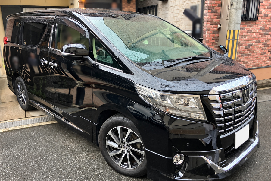 Black minivan parked on a wet city street, front three-quarter view with chrome grille and headlights.
